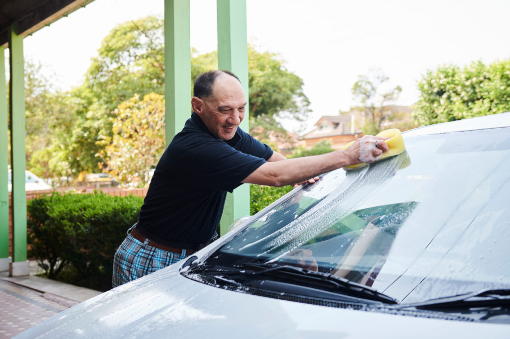 Guy in blue shirt washing car outside