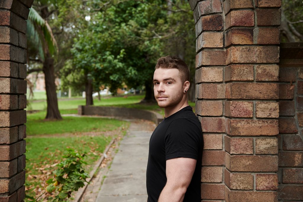 Guy in black t-shirt leaning against a wall outside