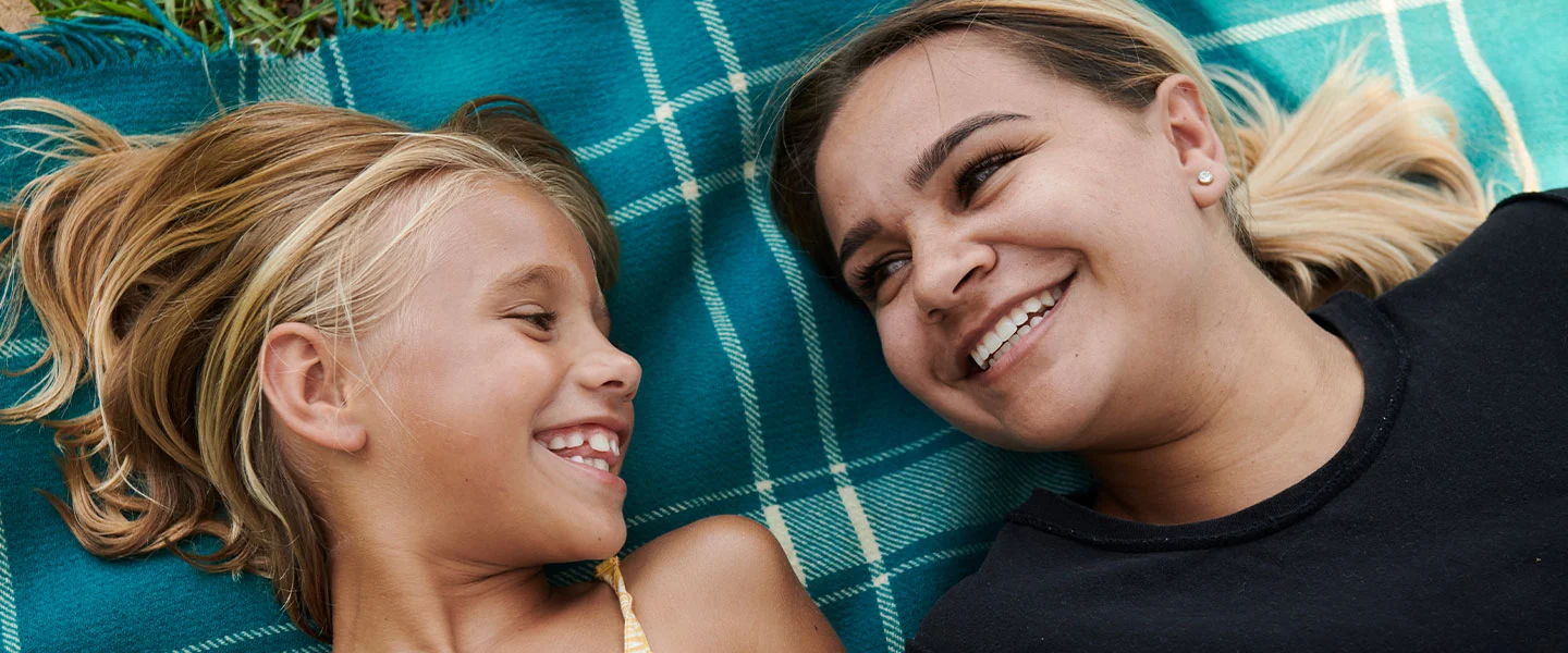 woman smiling at female child on picnic blanket