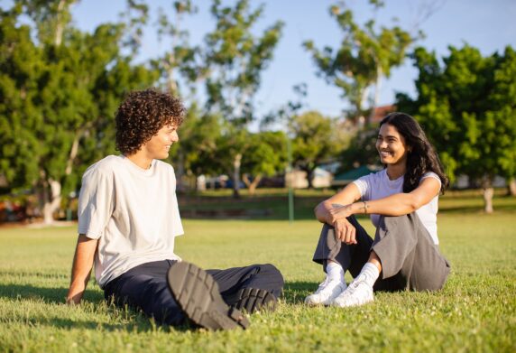 Two friends sitting on the grass smiling and talking