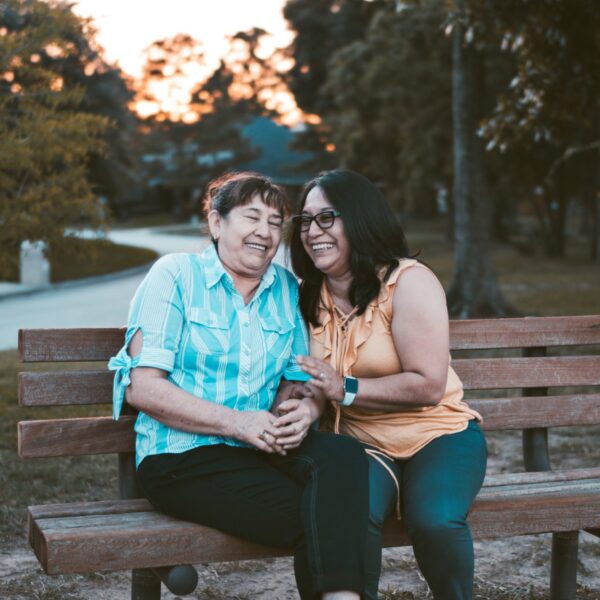 Two middle aged women sitting on park bench laughing together
