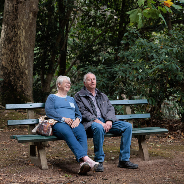 An older couple sitting on a bench in a forest looking at their surroundings