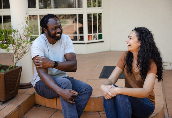 Two friends sitting on steps are chatting and laughing