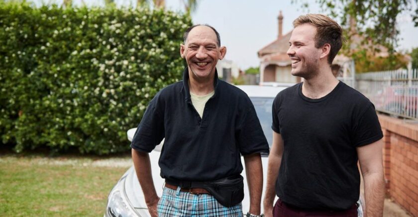 Two men standing in front of car smiling