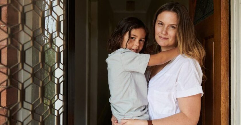 Mum holding daughter, smiling in doorway