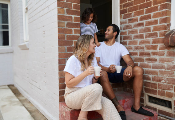 Mum dad and child sitting on house's front steps talking to each other