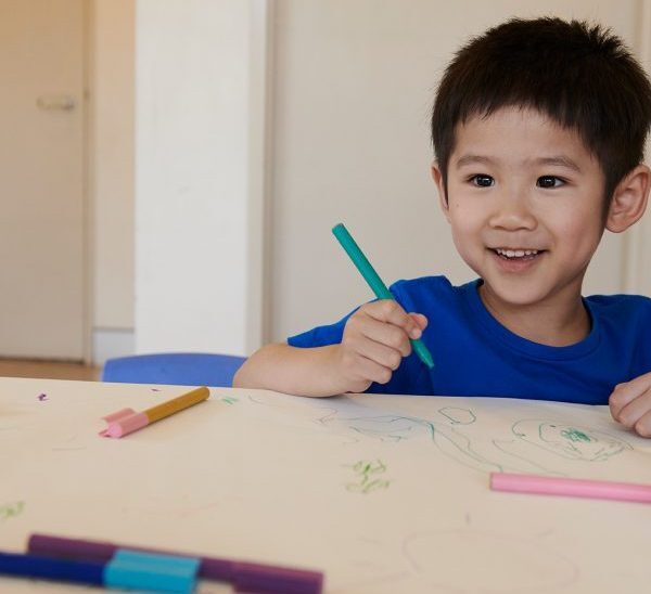 Young boy smiling at camera while drawing