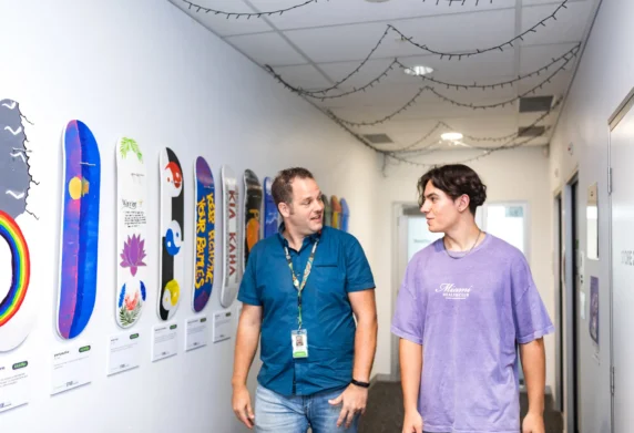 Two men walking down hallway past art on wall