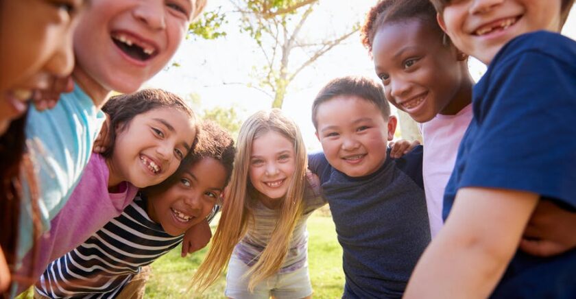 Low shot of children in a semi circle leaning in and smiling at the camera