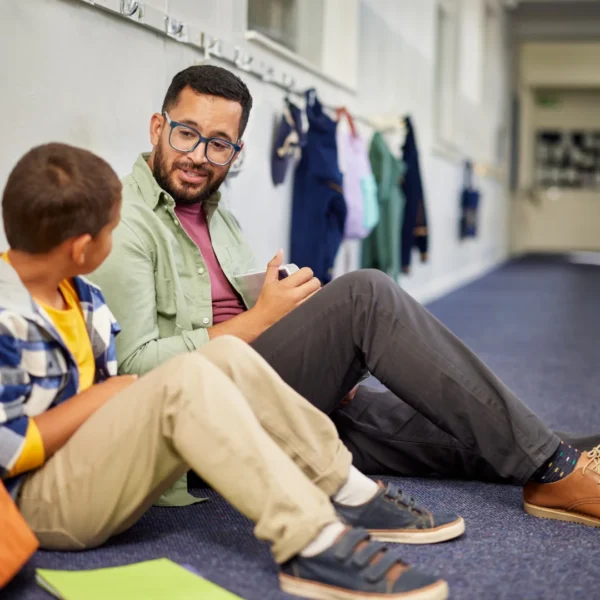 Young boy and man sitting on school hallway floor talking