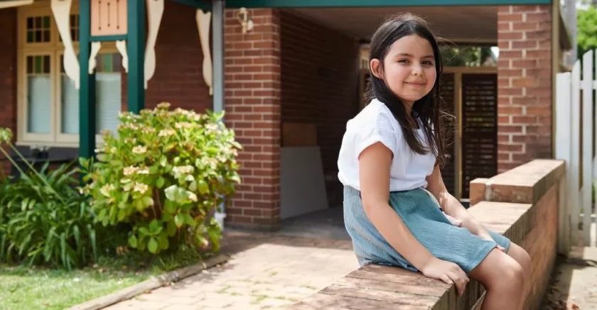 A female child sitting on steps of her house smiling at camera