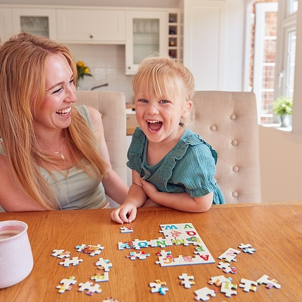 Mother and daughter giggling and having fun over a puzzle on the table