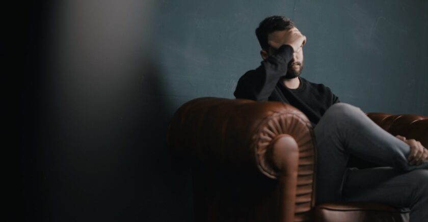 Man sitting on lounge looking sad with head in hand