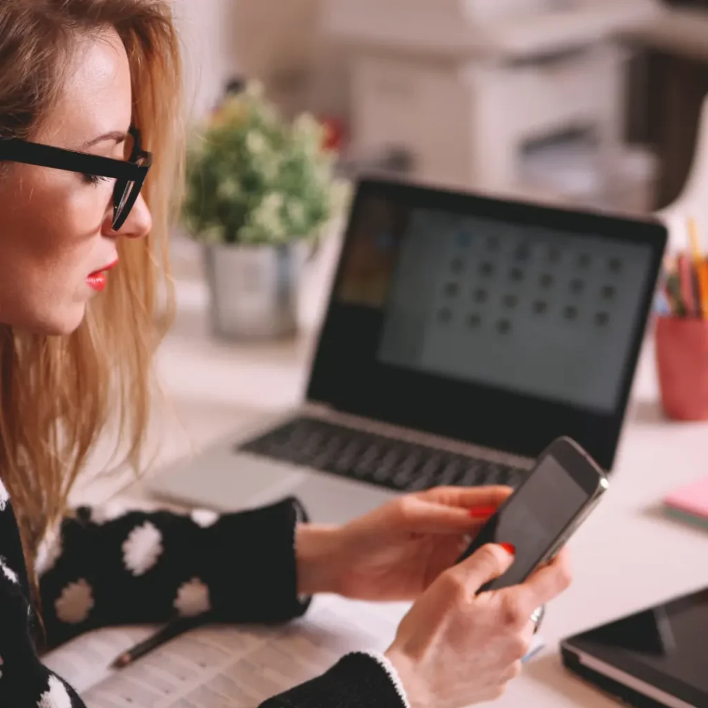 Woman on her phone typing next to her laptop
