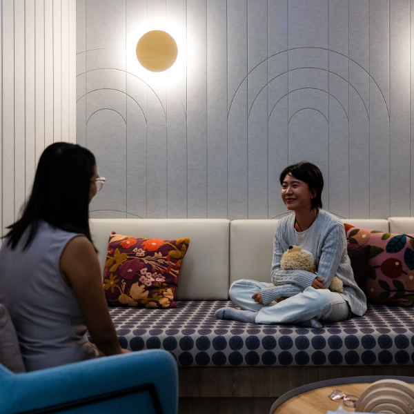 Person in sensory room with lights dimmed, shoes off hugging a teddy bear, relaxing on lounge having a chat