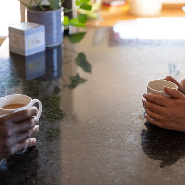 Two people having a conversation at kitchen bench over cups of tea