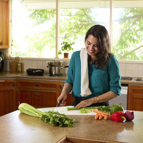Person in kitchen with towel over shoulder cutting up vegetables to cook