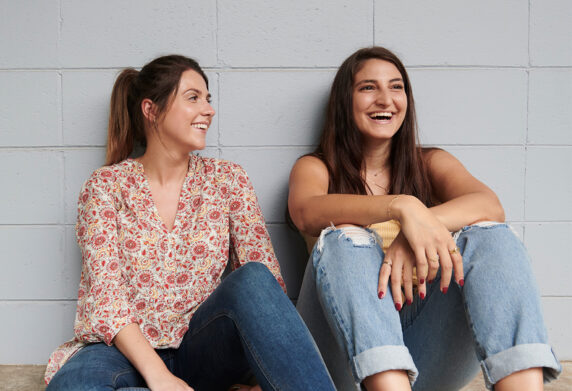 Two young women sit outside laughing together
