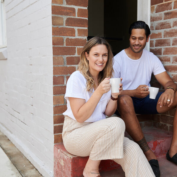 two adults sitting on steps drinking from mugs and smiling