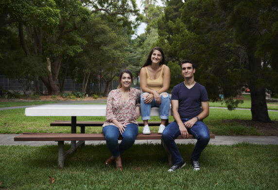 three youth people on park table and chair together smiling at camera