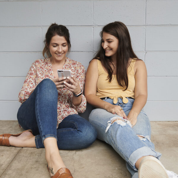 Two youth people leaning against wall look at mobile smiling