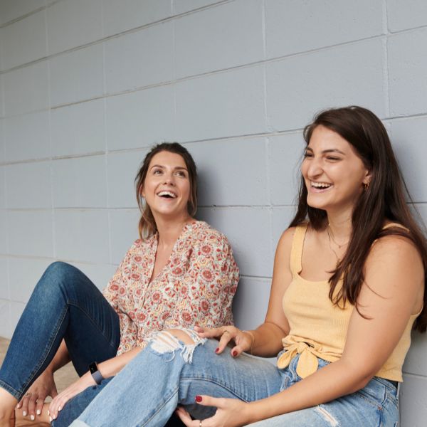 two youth people chatting and laughing sitting down against a wall