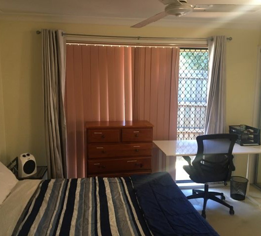 Bedroom with block out blinds, computer table, chair and double bed.